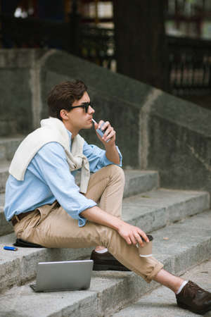 Young man with bad habits. Modern smoking youth. Unhealthy lifestyle, businessman on coffee break on urban backgroundの写真素材