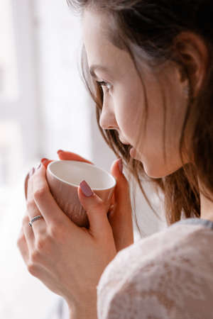 Sensitive morning with cup of delicious coffee. Meeting sunrise with favorite aromatic drink, enjoyment, calmness and romantic concept, close up woman side-view pictureの写真素材