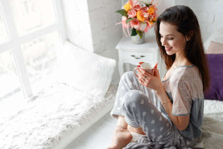 Smiling young woman with cup of aromatic tea at home. Waking up with positive energy charge for whole day, sunrise enjoyment and relaxation, refreshment drink conceptの写真素材