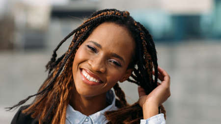 Merry African American female. Attractive model smiles. Happy smiley woman in selective focus outdoors, fashion hairstyle, happiness conceptの写真素材