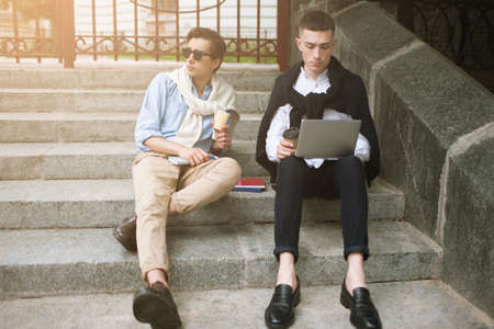 Social communication. Fashion youth outdoors. Two stylish male hipsters on coffee break, creative leisure time, technology conceptの写真素材