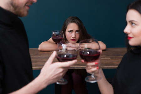 Sad alone female in bar. Jealousy backdrop. Love triangle, cheating relationships. Unhappy betrayed woman in focus on blue background, loneliness conceptの写真素材