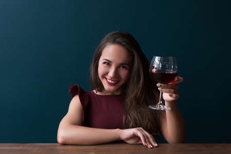 Happy smiling girl in bar with wine. Joyful female on blue background with free space, after work...
