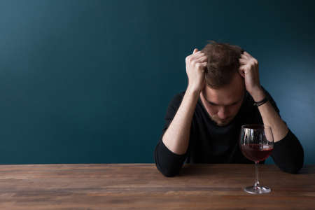 Despondent drunk young man in bar. Sad thoughtful male on blue background with free space, troubles in life with red wine. Unlucky date, bad habits, breakupの写真素材