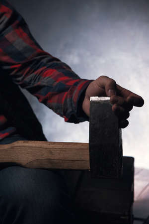 Maniac with sharp axe. Scary atmosphere. Wood chopper closeup, unrecognizable dangerous male with weapon in focus on foreground, grey background, danger conceptの写真素材