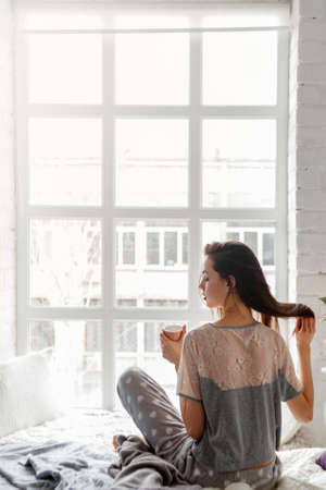 Sensual young woman with cup of tea at home, set her hair just waking up. Thoughtfulness and calmness, relaxation and perception concept. Good start of the day, back viewの写真素材