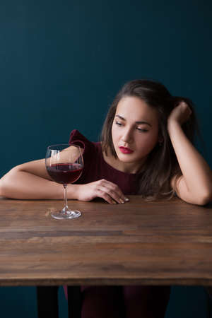 Thoughtful young female in bar. Melancholic mood. Sad woman with red wine on blue background with free space, unsuccessful romantic date. Problems in life, sadness conceptの写真素材