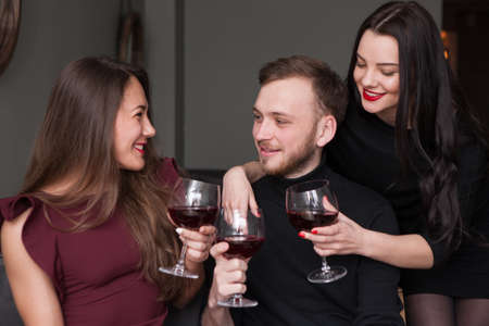 Female seduction at company party. Love triangle. Pleasant conversation, male surrounded by beautiful women with wine. Girl rivalry, romantic backgroundの写真素材