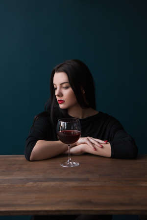 Lonely young female in bar. Melancholic mood. Sad woman with red wine on blue background with free space, unsuccessful romantic date. Problems in life, sadness conceptの写真素材
