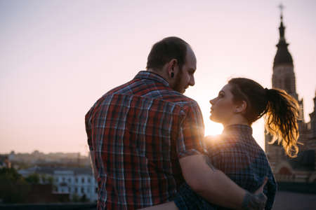 Romantic couple on roof in focus on foreground. Cuddling people together enjoying sunset. Sensitive look, stylish hipsters, urban background with free spaceの写真素材