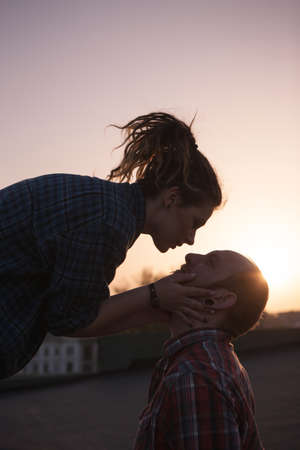 Gentle kissing couple on sunset backdrop closeup. Romantic date outdoors, hipsters in love in focus on foreground, feelings conceptの写真素材