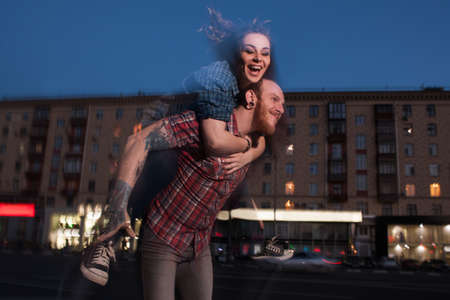 Happy flight. Love couple in motion. Flying smiley female, blurred urban background, cheerful man giving girl piggyback ride, fun conceptの写真素材