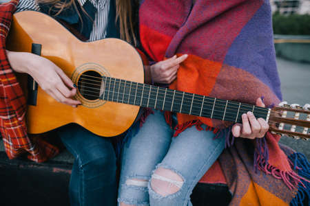 Playing guitar and meeting on roof, close up. Two girls studying music together, unusual places for rest and communication, sharing time in close and cheerful atmosphere conceptの写真素材