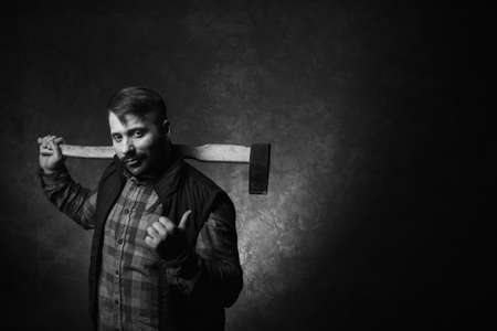 Woodsman with axe. Male strength. Adult worker man on dark background pointing at free space, confident lumberjack portrait closeup, rural conceptの写真素材