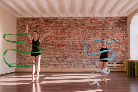 Young ballerinas rehearsal. Rhythmic gymnastics. Teenage sport, healthy teen lifestyle. Pretty girls with flying ribbons, dance class background with free space, ballet conceptの写真素材