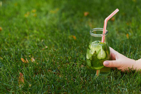 Healthy green detox drink on summer grass in hand. Fresh cold tea jar outdoors. Diet or healthy lifestyle conceptの写真素材