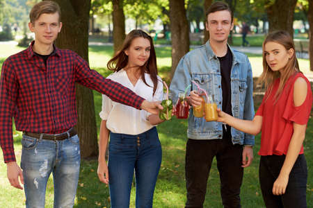 Healthy nutrition. Group of friends drinking fresh juice detox on green nature background. Youth lifestyle, vegetarian diet to go, fitness food, successful weight loss conceptの写真素材