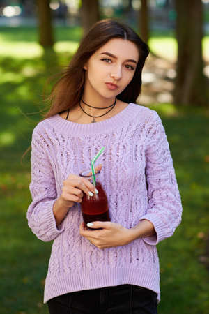 Healthy lifestyle. Cute young woman with fresh beet smoothie jar, on green nature background. Diet, detox in summer, well being and weight loss conceptの写真素材