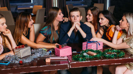 Seduction at Christmas party. Playful mood. Sexy females flirting with handsome man, young people company in club, New Year decoration, seductive conceptの写真素材