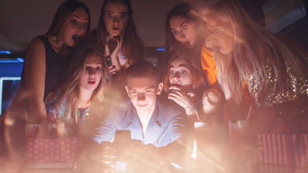 Surprising Christmas pictures on mobile phone. New Year miracle, females attention for young male. Night club background, amazing leisure time, surprise conceptの写真素材