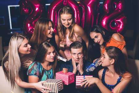 New Year party. Many females for man. Women attention with gifts for young tired male. Romantic mood at celebration, tiredness, spoiled child conceptの写真素材