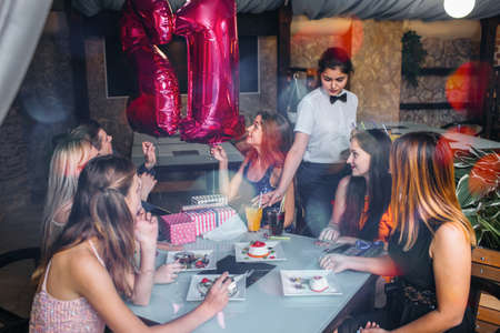 Birthday party celebration with friends. Happy youth company in cafe, modern leisure time. Joyful mood, waitress work, real festivity conceptの写真素材