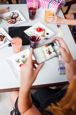 Modern lifestyle in cafe. Social media picture. Dinner in focus on background, mobile technology. Unrecognizable people company, food conceptの写真素材
