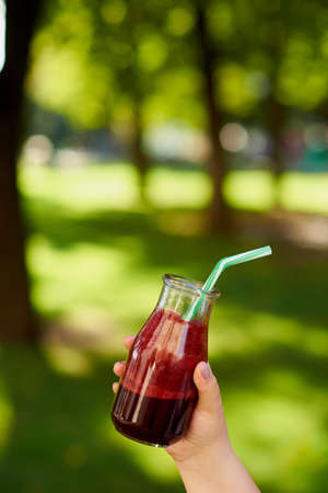 Healthy red detox drink in hand. Fresh beet smoothie jar outdoors. Diet or healthy lifestyle, well being and weight loss conceptの写真素材