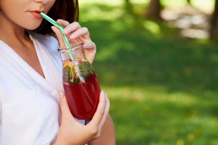 Young unrecognizable woman drinks healthy detox tea with juice on green park background. Superfoods,...
