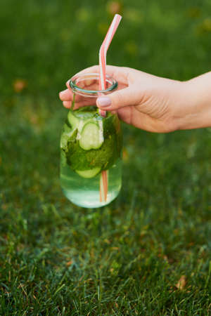Healthy green detox drink on summer grass in hand. Fresh cold tea jar outdoors. Diet or healthy...
