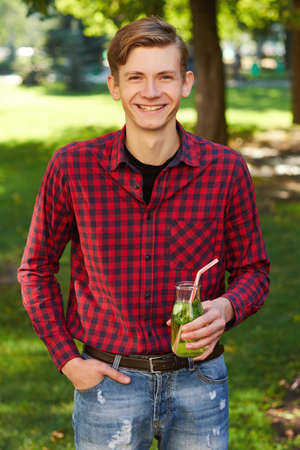 Healthy lifestyle. Happy young man with detox cocktail in summer, on green nature background. Diet, well being and weight loss conceptの写真素材