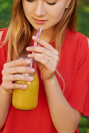 Young man drinks healthy detox smoothie with juice on green park background. Superfoods, health, summer freshness, vegetarian food conceptの写真素材