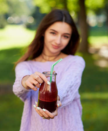Healthy lifestyle. Cute young woman with fresh beet smoothie jar, on green nature background. Diet,...