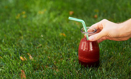 Healthy red detox drink in hand. Fresh beet smoothie jar outdoors. Diet or healthy lifestyle, well being and weight loss conceptの写真素材