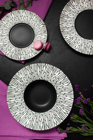 Three fancy plates on black background. Creative restaurant table setting with flowers and purple...
