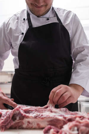 Restaurant chef in black apron cutting fresh lamb meat in the kitchen. Ingredient preparation before cooking a delicious mealの写真素材