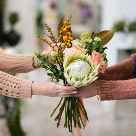 Safe and quick flower bouquet delivery for someone you love. Women hands holding a creative arrangement of roses dahlia and berriesの写真素材