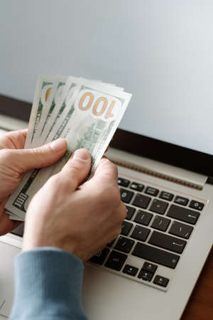 Online casino gambling. Man holding money and placing virtual bets using laptop. Luck success and winning conceptの写真素材