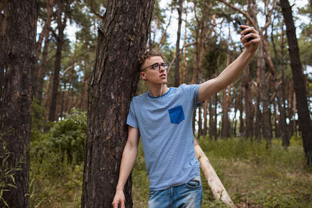 Self-confident man does selfie by the phone in the forest. Alone on the nature. Traveler lifestyle.の写真素材