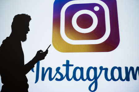 Ukraine, Kharkiv, 24.10.2017. Instagram. Social network designed for photo and video sharing, business promotion and online income. Silhouettes of people using phones with insta logo in the backgroundのeditorial素材
