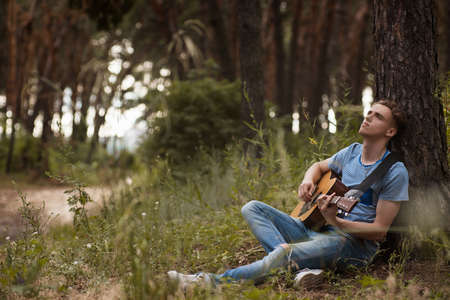 Pensive man playing guitar forest concept. Alone on the nature. Lifestyle of artist.の写真素材