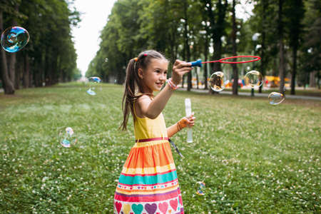 Impressed little girl blows bubbles in the park. Delights of childhood.