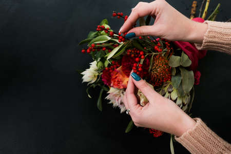 Woman creating autumn flower arrangement on dark background. Bouquet design and composition art ikebana.の写真素材
