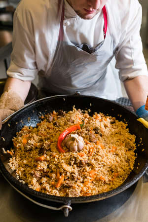 Chef cooking plov in the kitchen. Traditional famous Uzbek rice meal.の写真素材