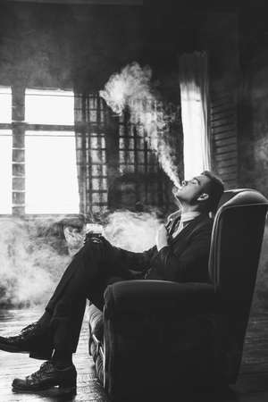 Man vaping fumes and drinking alcohol to relax. Enjoyment satisfaction and chilling conceptの写真素材