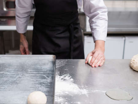 Baker works with dough on a metal work surface. Professional cook making rolls or buns