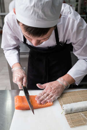 Chef cuts salmon or trout when preparing philadelphia sushi rolls.の写真素材