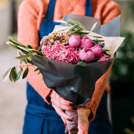 Woman holding a bouquet of peonies and hydrangeas in a craft wrapping that she made. Small floral business owner. Female power startup conceptの写真素材