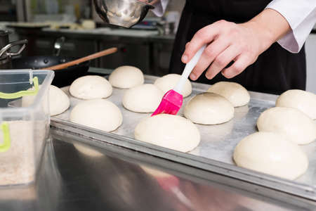 It is where a burger begins. A cook greasing hamburger rolls before putting them in the oven and...