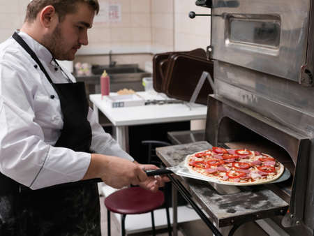 Cheff cooking pizza and putting it in the oven to bake. One more step and magnificent italian dish will be readyの写真素材
